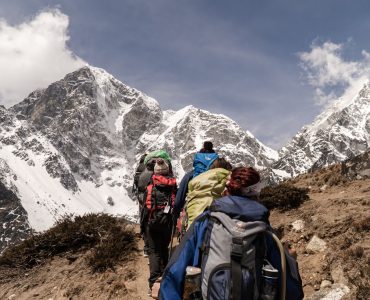 Nữ trekker chống gậy đứng trên đỉnh núi tuyết nhìn xuống thung lũng 4000m