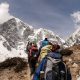 Nữ trekker chống gậy đứng trên đỉnh núi tuyết nhìn xuống thung lũng 4000m