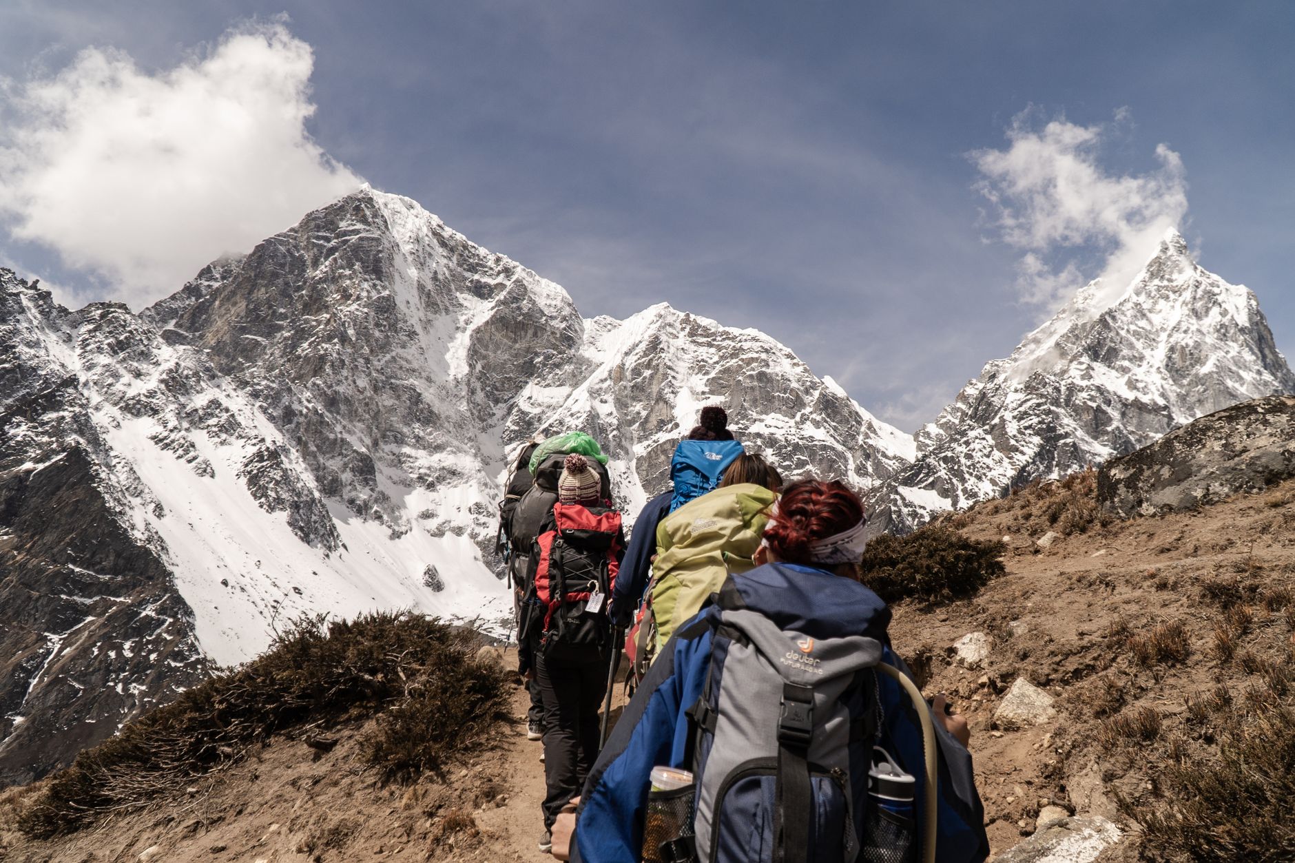 Nữ trekker chống gậy đứng trên đỉnh núi tuyết nhìn xuống thung lũng 4000m